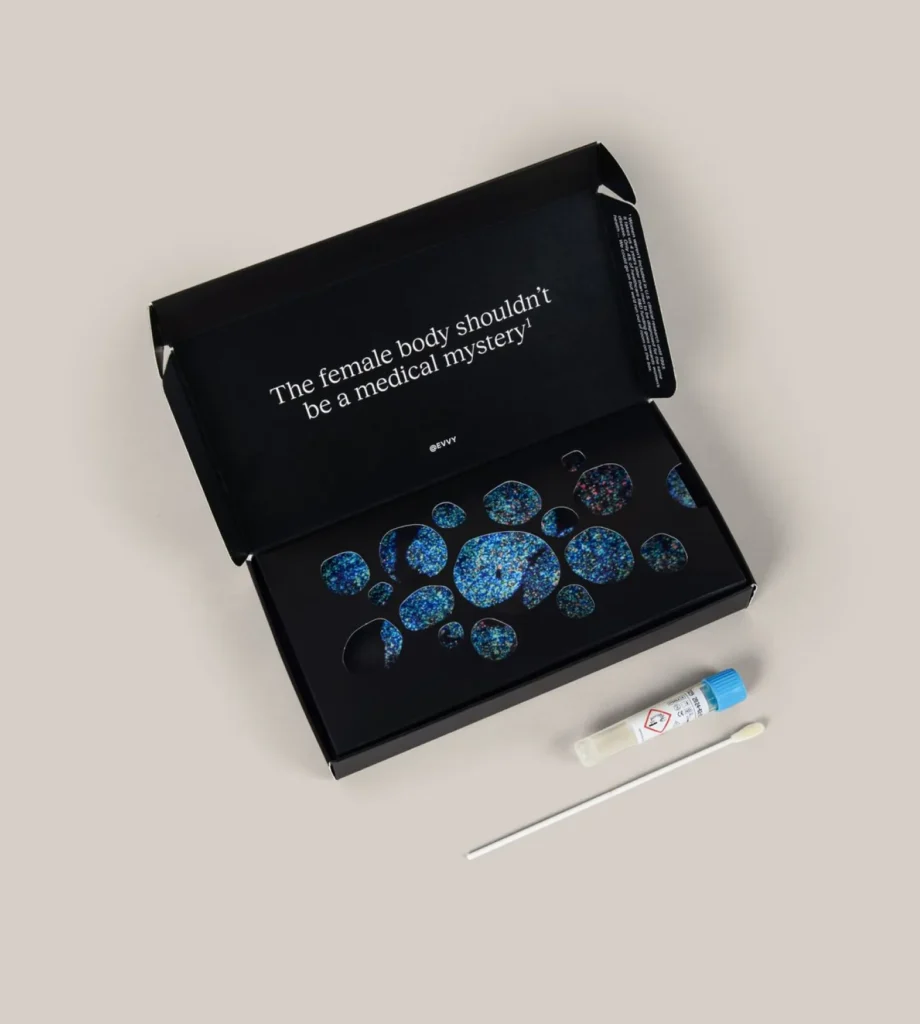 An open black box with the text "The female body shouldn't be a medical mystery!" contains a kit with blue patterned items, next to a swab and a sample vial on a beige surface. , Kiara Health Fertility