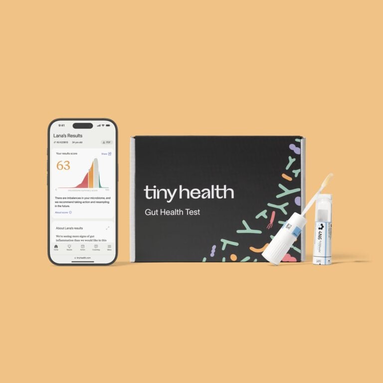 A Tiny Health Gut Health Test kit displayed with a swab, test tube, and a smartphone showing gut health test results, all set against a light tan background. , Kiara Health Fertility