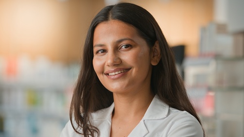 A woman wearing a white coat smiles while standing in a brightly lit indoor setting with shelves in the background, creating an inviting scene perfect for a Landing Page 7.2. , Kiara Health Fertility